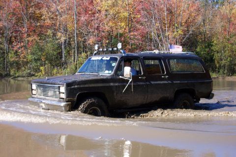 1979 Ford Bronco - This black SUV, possibly a 1979 model, navigates through a muddy off-road course with autumn foliage in the background.