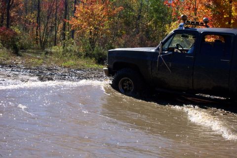 1979 Ford Bronco - Pickup truck navigates muddy water during an off-road excursion in the fall.