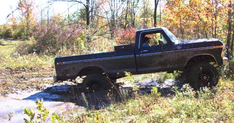 1979 Ford Bronco - A lifted pickup truck navigates a muddy trail surrounded by autumn foliage.