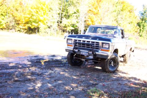 1979 Ford Bronco - A Ford pickup truck navigates a muddy, off-road path with trees in the background.