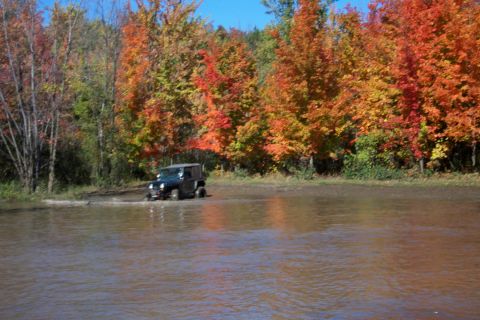 1979 Ford Bronco - Jeep Wrangler navigates through water during autumn.