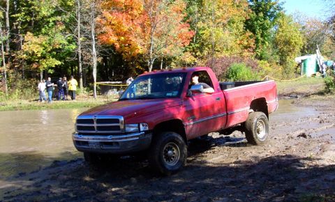 1979 Ford Bronco - A red Dodge Ram pickup truck navigates a muddy off-road course during autumn.
