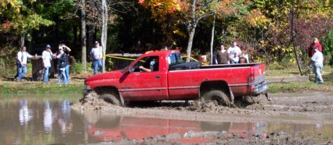 1979 Ford Bronco - A red pickup truck is stuck in a muddy area with onlookers.
