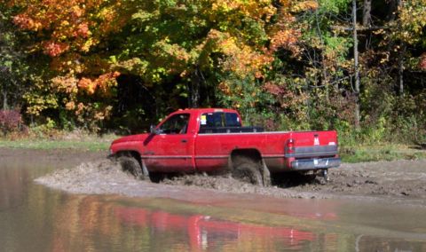 1979 Ford Bronco - A red pickup truck navigates through a muddy terrain during autumn.