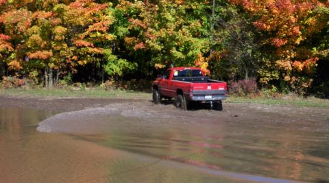 1979 Ford Bronco - A red pickup truck navigates through a muddy area during autumn.