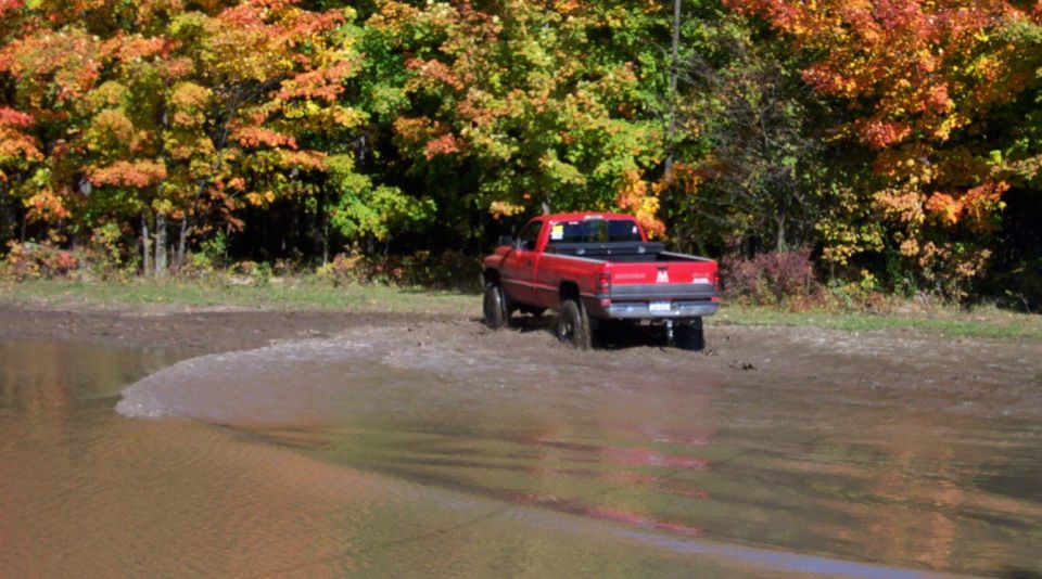 Red pickup truck stuck in mud with fall foliage in the background
