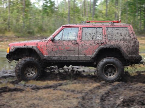 1989 Ford Bronco - Red Jeep Cherokee XJ navigating a challenging muddy off-road course.