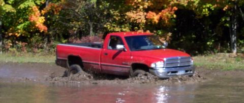 1979 Ford Bronco - A red pickup truck navigates through a muddy area with fall foliage in the background.