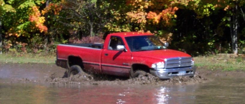 Red pickup truck driving through mud, front quarter view