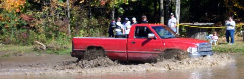 1979 Ford Bronco - A red pickup truck navigates a muddy obstacle course with spectators watching from the side.