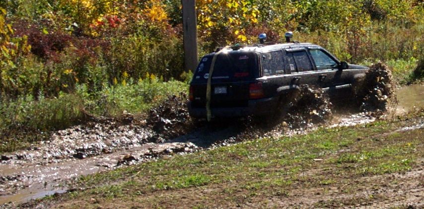 Black SUV splashing through a muddy trail with trees in the background