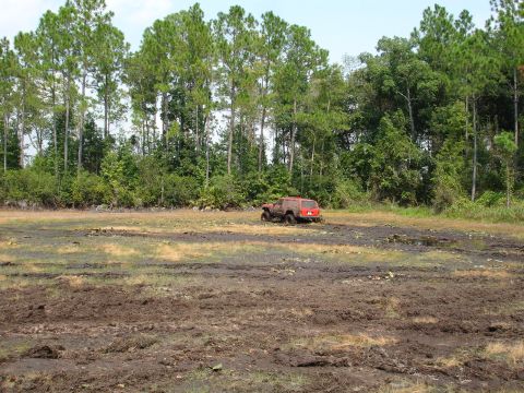 1989 Ford Bronco - Red SUV stuck in mud, with trees in the background.