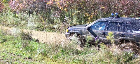1979 Ford Bronco - A Jeep Grand Cherokee navigates a muddy off-road trail surrounded by autumn foliage.