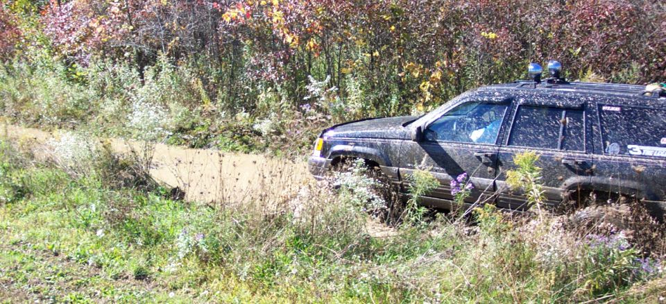 Black Jeep Grand Cherokee stuck in mud on a trail, with trees and foliage in the background