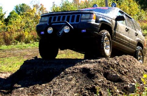 1979 Ford Bronco - This Jeep Grand Cherokee is shown navigating an off-road obstacle, with its front grille and auxiliary lights clearly visible.