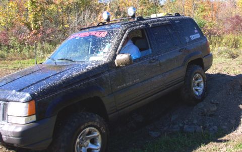 1979 Ford Bronco - A muddy Jeep Grand Cherokee navigates an off-road trail with autumn foliage in the background.