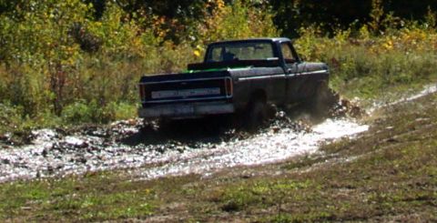 1979 Ford Bronco - This black pickup truck navigates a muddy trail, kicking up water and dirt.