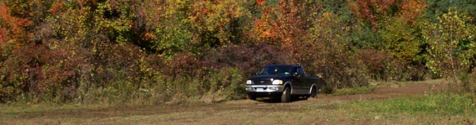 Black pickup truck parked on a dirt road with autumn foliage in the background