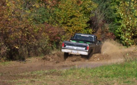 1979 Ford Bronco - A black pickup truck navigates a muddy trail, kicking up water and dirt.