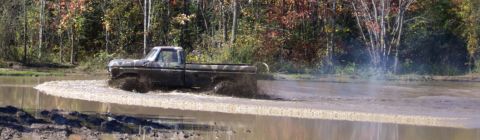 1979 Ford Bronco - A classic Ford pickup truck navigates a muddy off-road course, sending water and mud flying.
