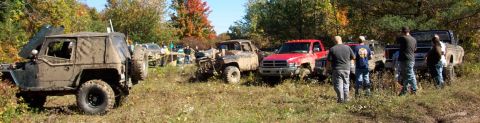 1979 Ford Bronco - Several off-road vehicles are parked in a grassy, wooded area with fall foliage visible in the background.