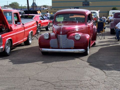 1972 Ford Ranchero - A shiny red 1940s Chevrolet coupe is displayed at a car show with other vehicles.