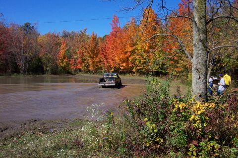 1979 Ford Bronco - Truck navigates a water obstacle surrounded by vibrant autumn trees.