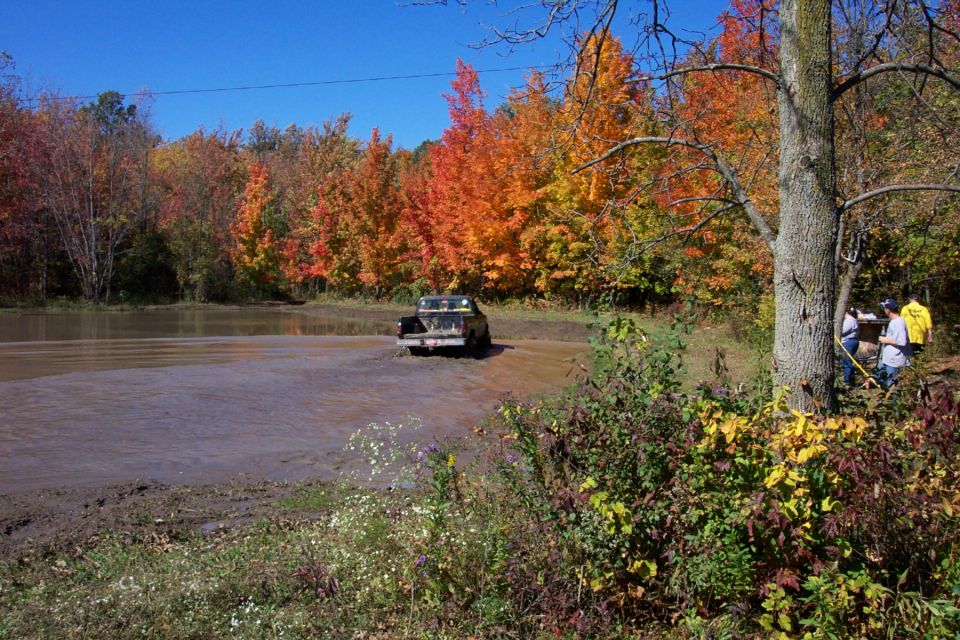 Truck driving through a muddy water crossing with fall foliage in the background