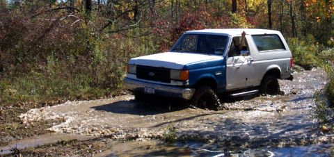 1979 Ford Bronco - A two-tone Ford Bronco navigates a muddy trail during autumn.
