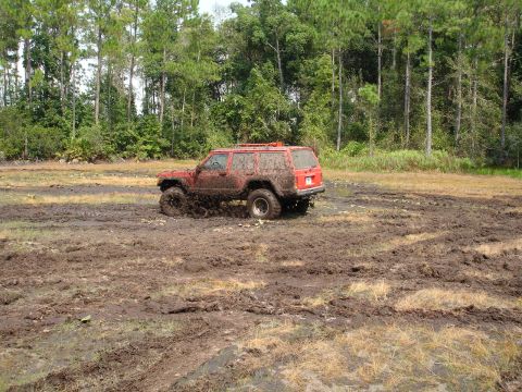 1989 Ford Bronco - This red Jeep Cherokee XJ is stuck deep in the mud, with its tires churning up the wet earth.