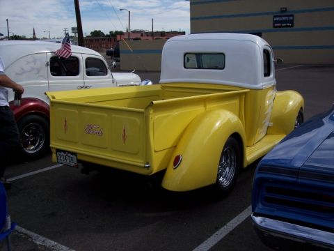 1972 Ford Ranchero - A yellow Ford pickup truck is parked next to a blue car and a white van with an American flag.