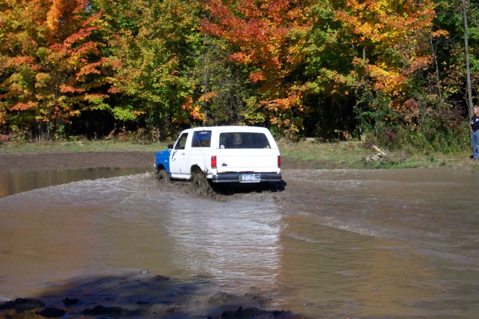 1979 Ford Bronco driving through a muddy puddle with fall foliage in the background