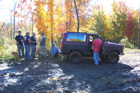 1979 Ford Bronco - A group of people and a dog stand around a purple and black Ford Bronco in a muddy, wooded area during autumn.