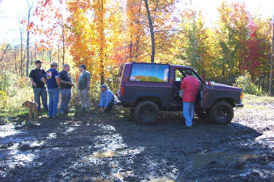 Purple and black Ford Bronco with off-road tires stuck in mud, people standing around