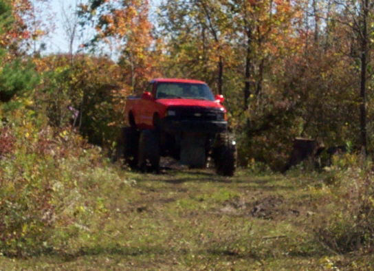 Red lifted pickup truck with large tires on a dirt path