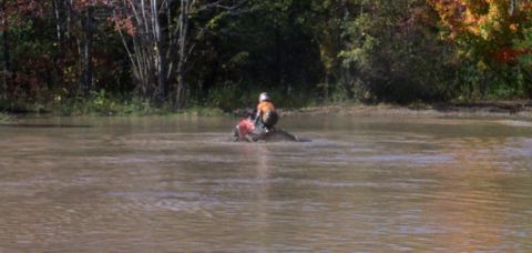 1979 Ford Bronco - ATV rider navigates through a shallow body of water surrounded by autumn foliage.