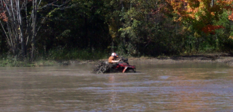 Red ATV stuck in muddy water with trees in background
