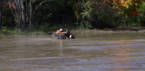 1979 Ford Bronco - ATV navigates through a body of water with trees lining the shore.