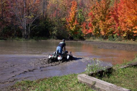 1979 Ford Bronco - An all-terrain vehicle splashes through muddy water surrounded by colorful fall foliage.