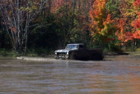 1979 Ford Bronco - A vintage Ford pickup truck navigates a muddy water crossing amidst autumn trees.