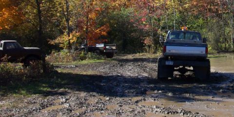 1979 Ford Bronco - Multiple trucks navigate a challenging muddy terrain surrounded by fall foliage.