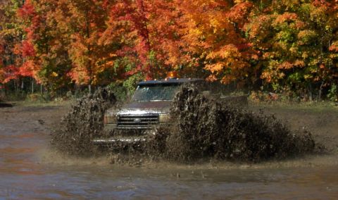 1979 Ford Bronco - A truck navigates a muddy obstacle course amidst vibrant autumn trees.