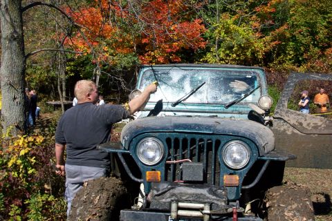 1979 Ford Bronco - A person cleans the muddy windshield of a Jeep Wrangler while another Jeep is visible to the right.
