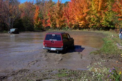 1979 Ford Bronco - Two SUVs navigate a muddy obstacle course during autumn.