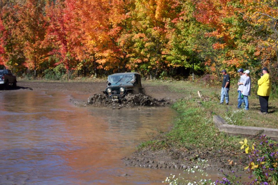 Green off-road vehicle splashing through mud with fall foliage in background
