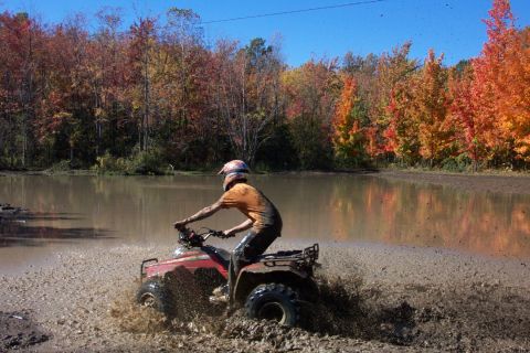 1979 Ford Bronco - A rider on a red ATV navigates a muddy trail surrounded by colorful fall foliage.