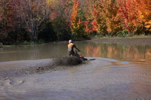1979 Ford Bronco - An ATV rider kicks up mud while navigating a watery trail surrounded by autumn trees.