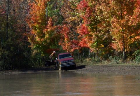 1979 Ford Bronco - Red pickup truck and ATV in muddy terrain during autumn.