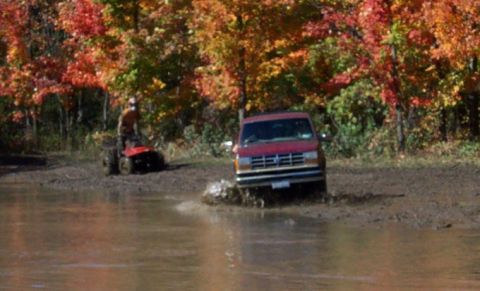 1979 Ford Bronco - A red van navigates a muddy trail during autumn, with a person on a lawnmower nearby.