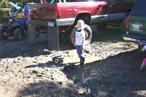 1979 Ford Bronco - A muddy scene with a boy and toy trucks, while larger vehicles and an ATV are parked nearby.